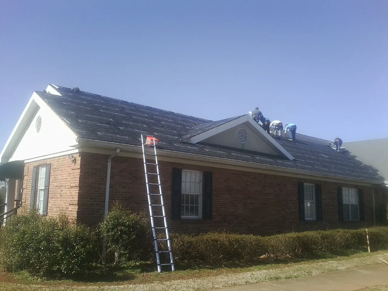 Crew tearing shingles off a brick ranch roof with a ladder set — Emergency Roof Repair work by our crew in Reedsville