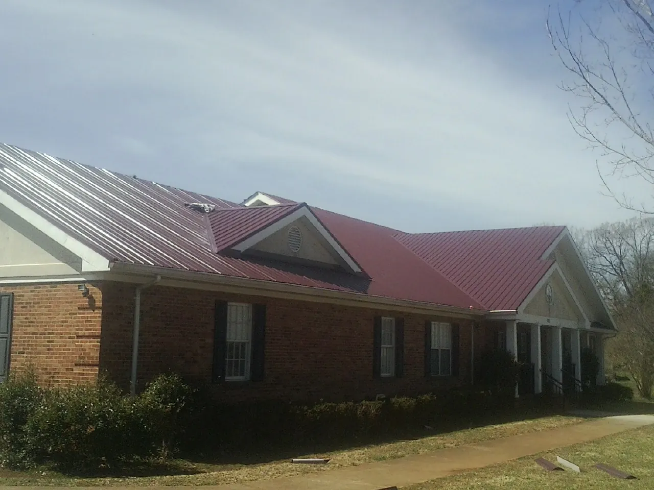 Red metal roof with gabled entries on a long brick building, from a Hail Damage Roof Repair job in Reedsville
