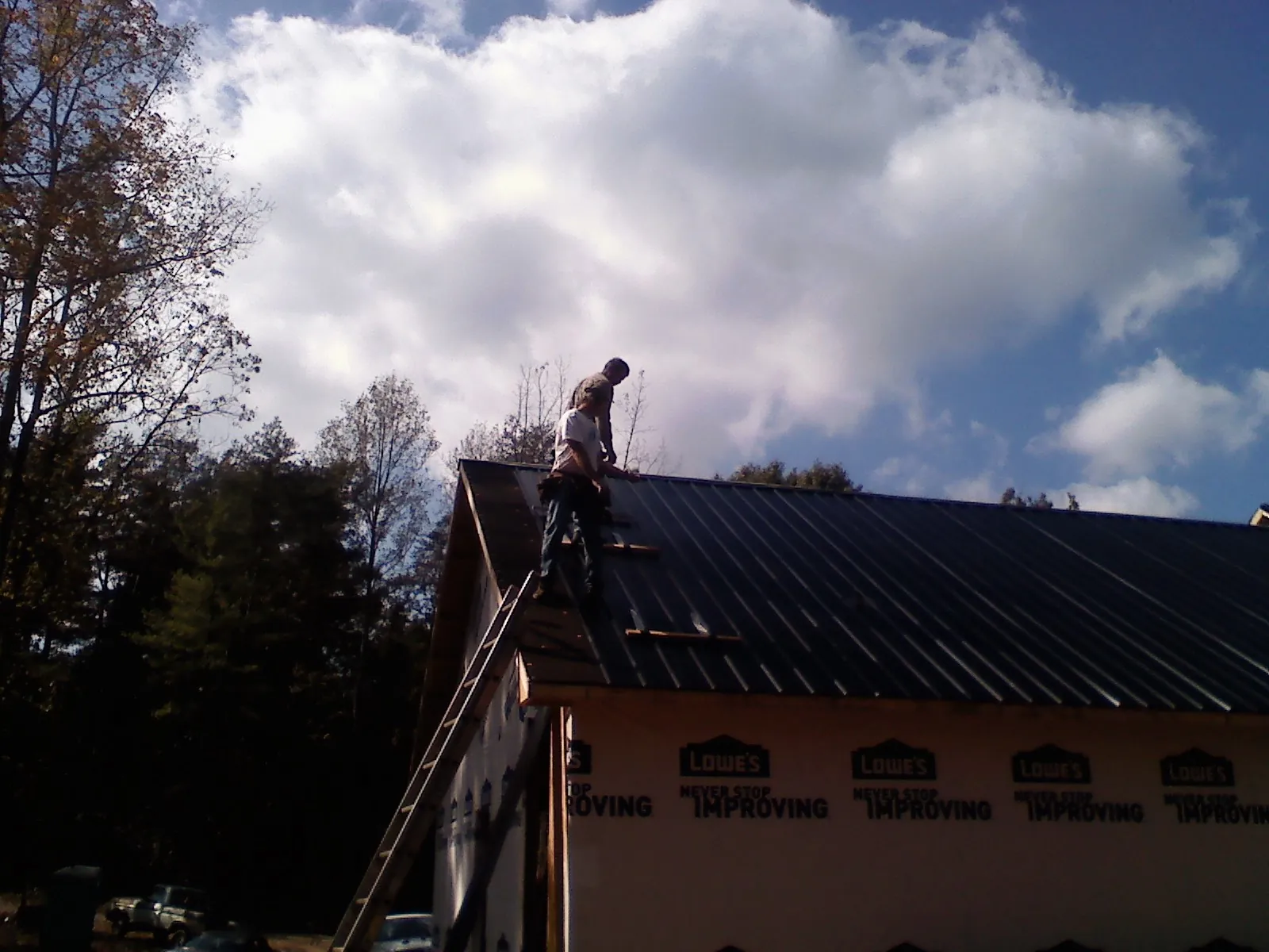 Roofer fastening dark metal panels high against a cloudy sky, from a Roof Inspection job in Reedsville