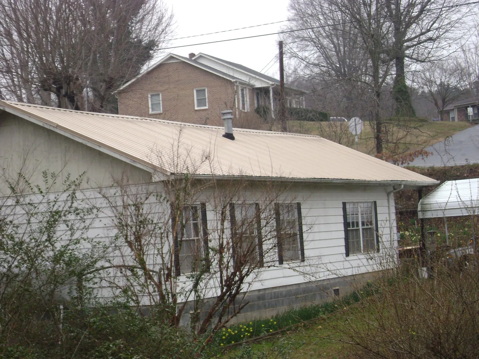 Tan metal roof on a white sided house set into a hillside — Commercial Roofing by Roofing Brothers in Reedsville